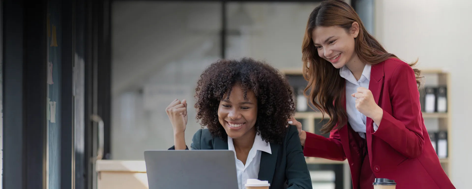 Two women celebrating in front of a laptop in an office setting